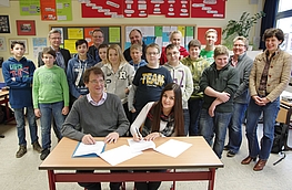 Andreas Ennen und Eda Medet (vorn) unterzeichneten den Vertrag im Beisein von Bürgermeister Otto Steinkamp (3. von links), Schulleiter Thomas Behning (5. von links), Gabriele Brümmer (rechts) sowie Schülern und Lehrern der Klasse 8a.