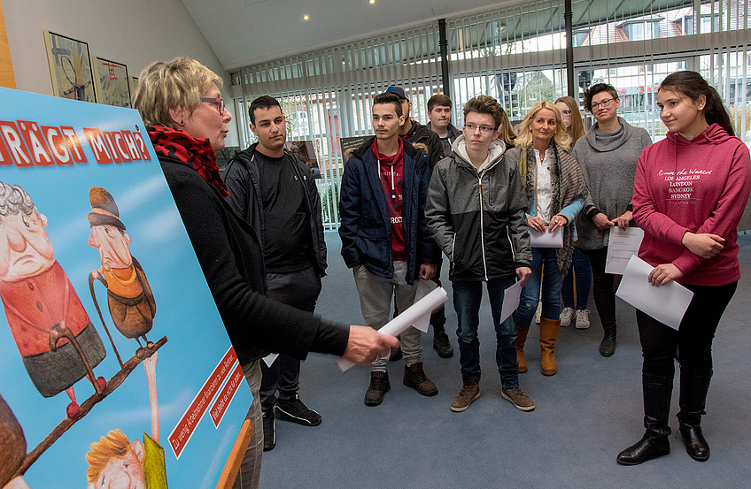 Kornelia Böert (links) erläutert die Motive der Ausstellung und diskutiert diese mit den Schülerinnen und Schülern.