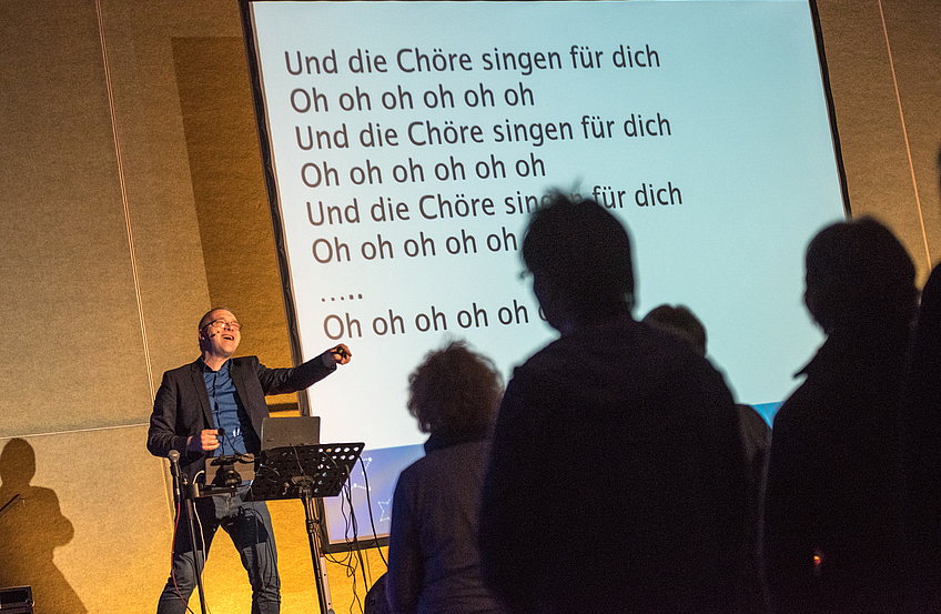 Die Chöre singen nicht nur für ihn, sondern vor allem für sich selbst – David Rauterberg unterstützt auf der Bühne mit Musik und Text.