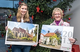 Kristina Niemann und Gisela Schawe (von links) präsentieren den Fotokalender der Gemeinde Wallenhorst, den sie an der Infotheke im Rathaus anbieten.