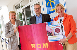 Künstlerin Vera Degener, Wallenhorsts Wirtschaftsförderer Frank Jansing und Birgit Ludwig-Trienen (Reise-Treff Ludwig) mit einem Bild und dem Plakat zur Schaufenstergalerie.