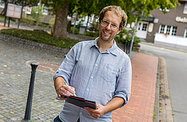 Stefan Brune steht mit einer Checkliste auf einem Gehweg.