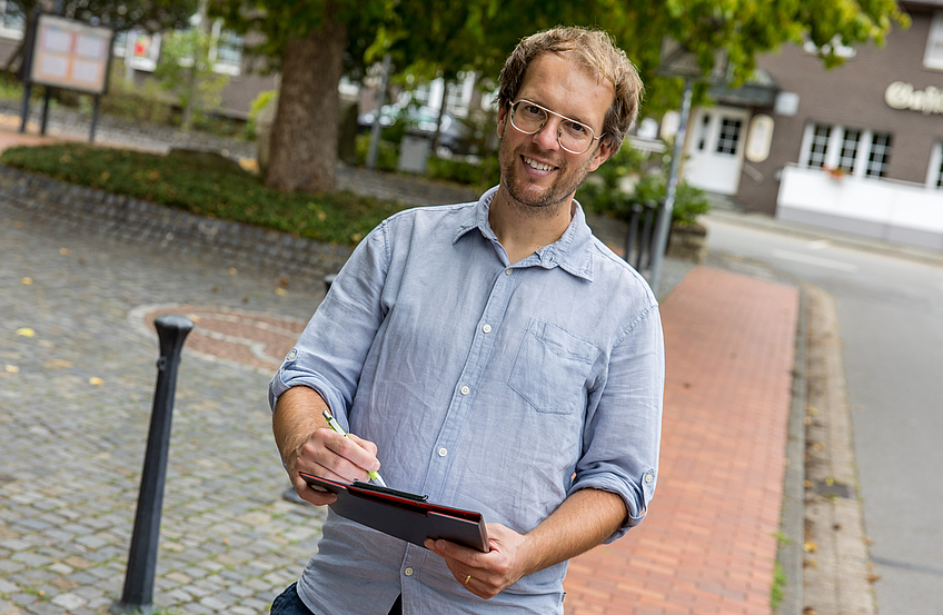 Stefan Brune steht mit einer Checkliste auf einem Gehweg.